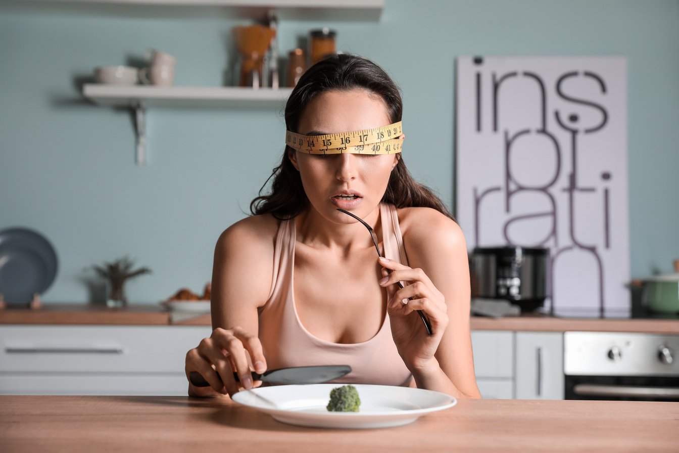 Young Woman Suffering from Anorexia Eating Broccoli