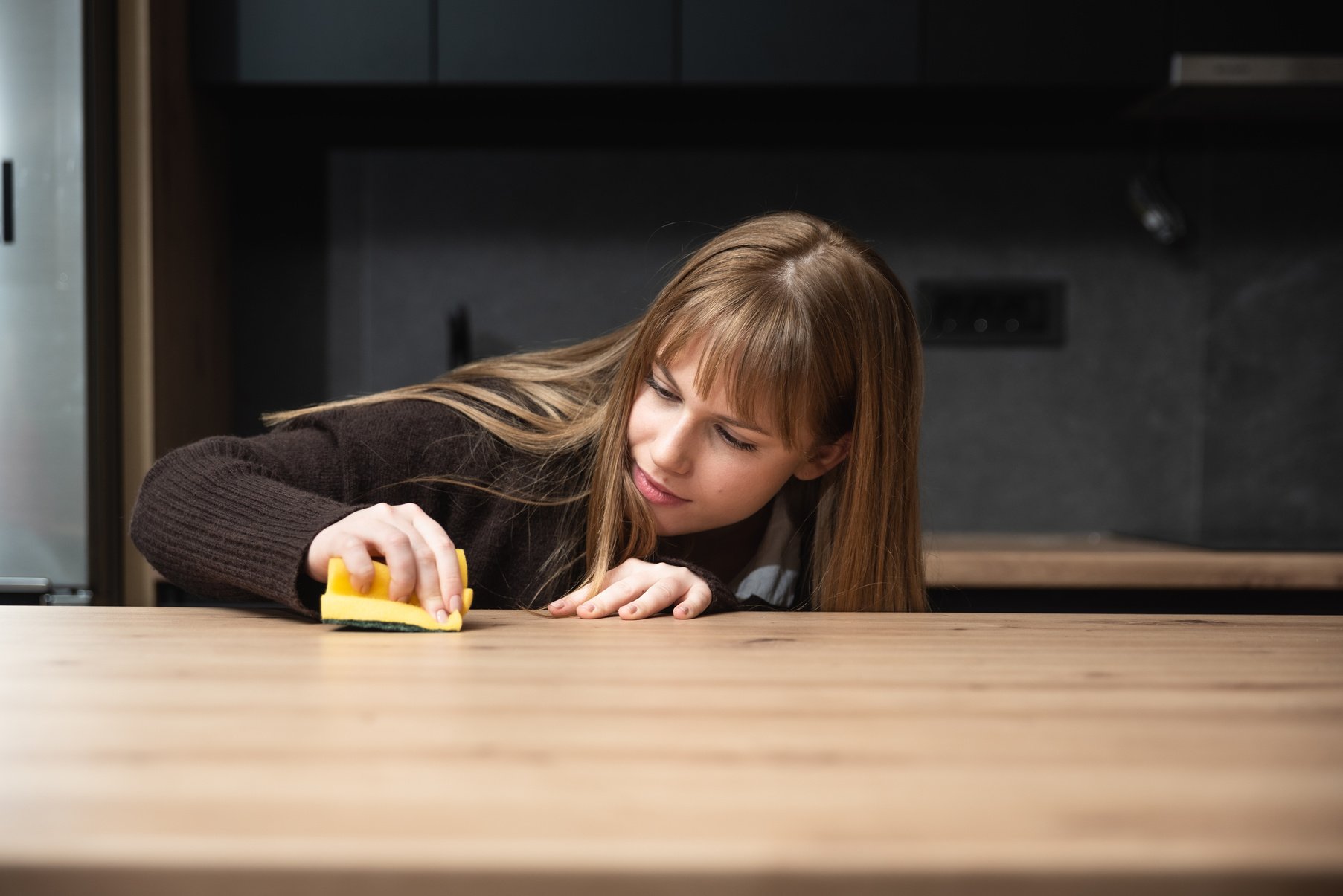 Young woman suffers from depression after a breakup or divorce and from obsessive compulsive disorder OCD cleans kitchen cook top to calm her nerves. Serious stressed female rubbing the home